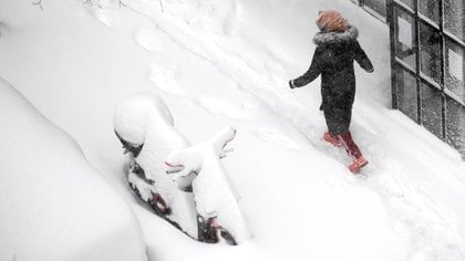 Una mujer pasa caminando entre la nieve, que cubrió una moto (AP Photo/Paul White)