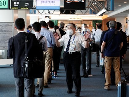 Un miembro del personal de All Nippon Airways que lleva una máscara protectora y un protector facial pide a los pasajeros que mantengan una "distancia social" mientras hacen cola para embarcar 