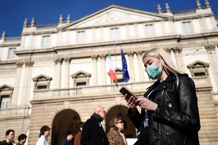 Una mujer con una mascarilla mira su teléfono fuera del Teatro alla Scala, cerrado por las autoridades debido a un brote de coronavirus, en Milán, Italia, 24 de febrero de 2020. REUTERS/Flavio Lo Scalzo