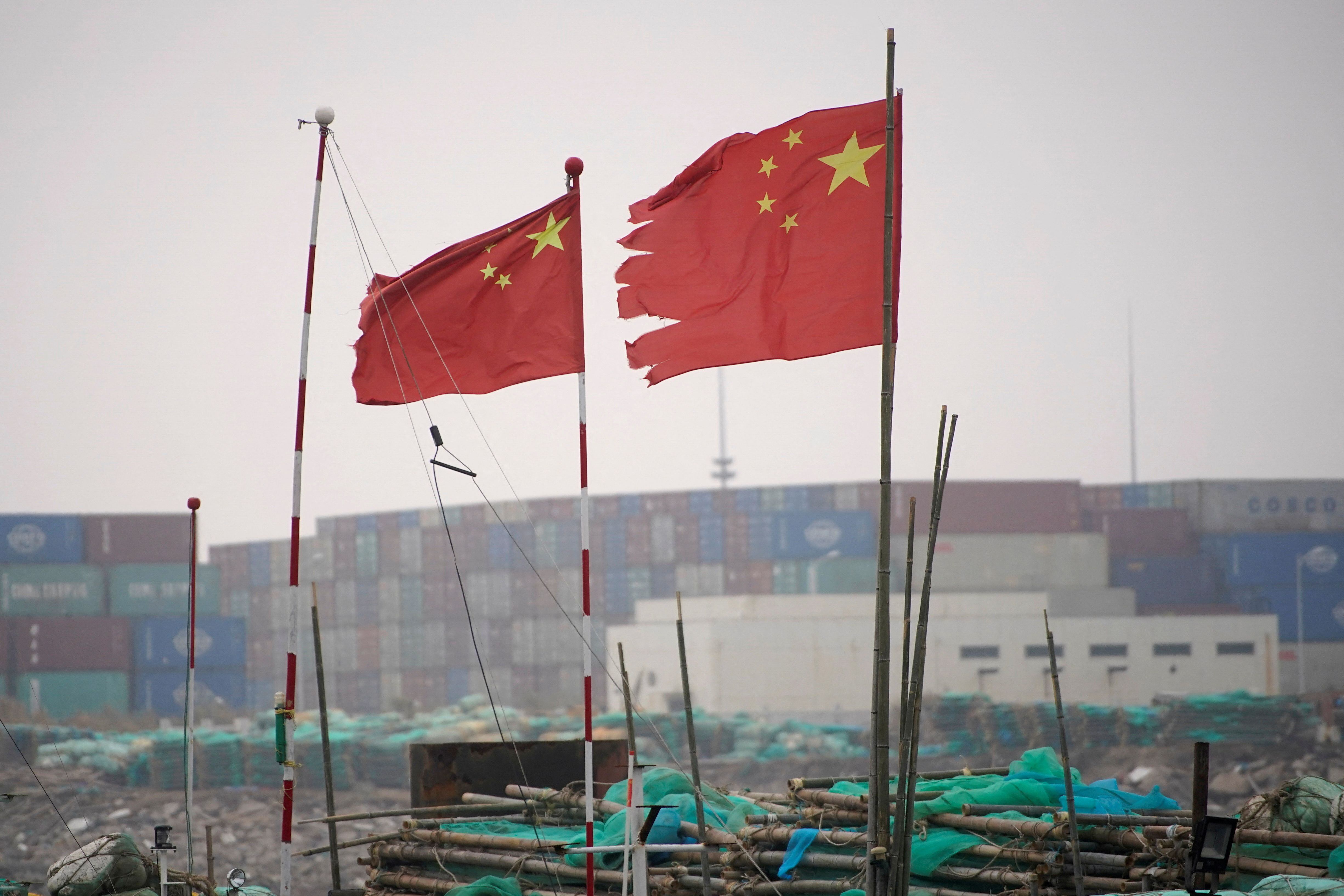 FOTO DE ARCHIVO: Banderas chinas ondean cerca de contenedores apilados en el puerto de aguas profundas de Yangshan, en Shanghái, China, en enero de 2022 (Reuters)
