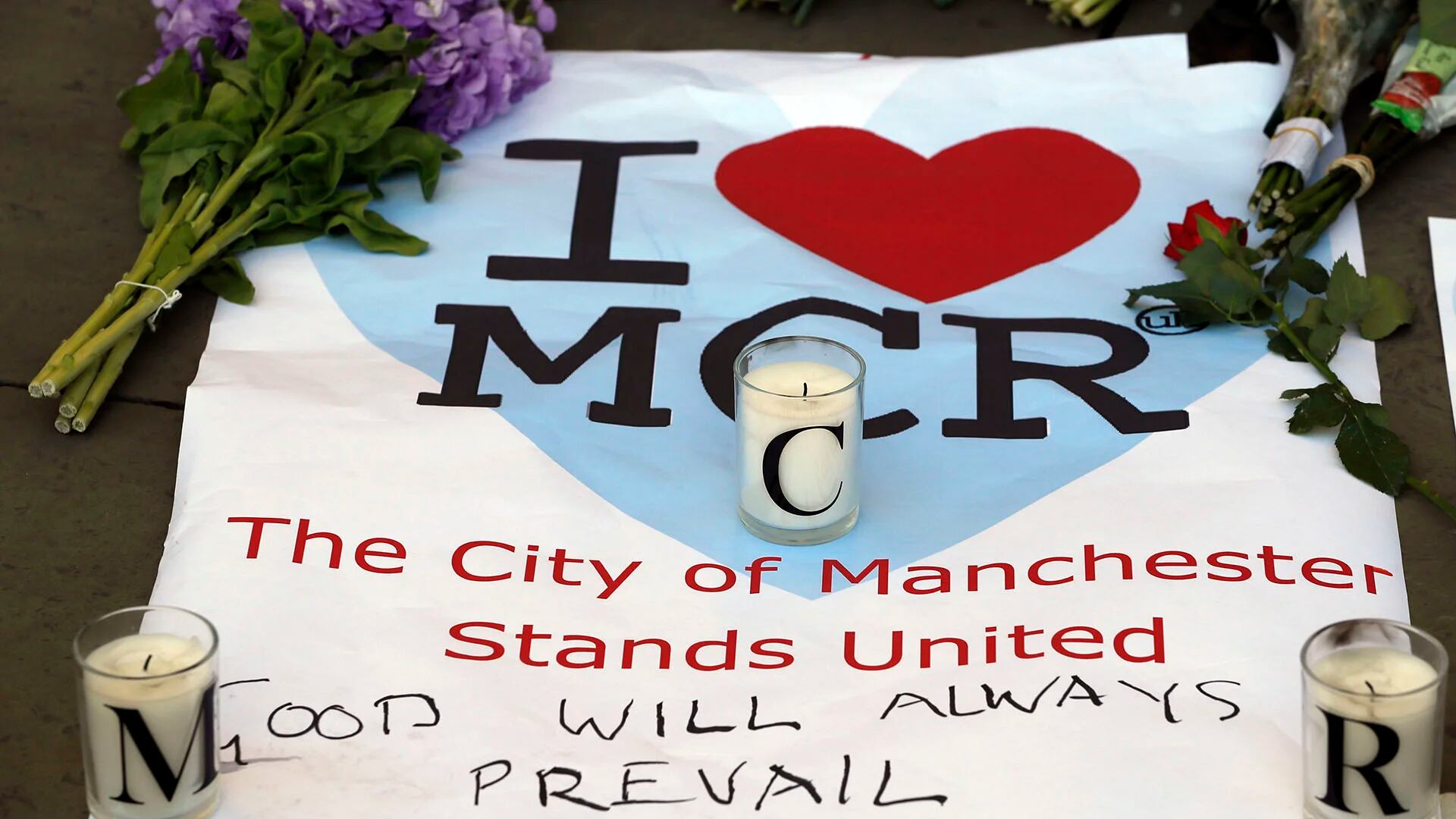 “La ciudad de Manchester permanece unida”, se puede leer en una bandera tendida sobre el piso con flores y velas (AP)