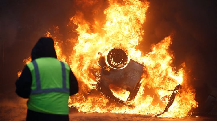 Un manifestante con su chaleco amarillo, delante de un automóvil incendiado y volcado en París (Reuters)