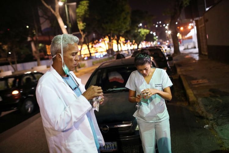 Los doctores Carlos Martínez y María Martínez comen un refrigerio mientras esperan en la fila para obtener combustible en una gasolinera, durante una cuarentena a debido al brote de la enfermedad por coronavirus (COVID-19), en Caracas. 7 de abril 2020. REUTERS/Manaure Quintero