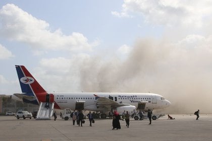 Gente camina sobre la pista mientras el polvo y el humo se elevan después de que  explosiones golpearan el aeropuerto de Aden, a la llegada del gobierno yemení recién formado a Aden (REUTERS/Fawaz Salman)