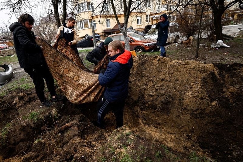 Serhii Lahovskyi, de 26 años, y otros residentes llevan el cuerpo de Ihor Lytvynenko, quien según los residentes fue asesinado por soldados rusos, después de que lo encontraron junto al sótano de un edificio, para enterrarlo en el jardín de un edificio residencial, en medio de la invasión de Rusia a Ucrania