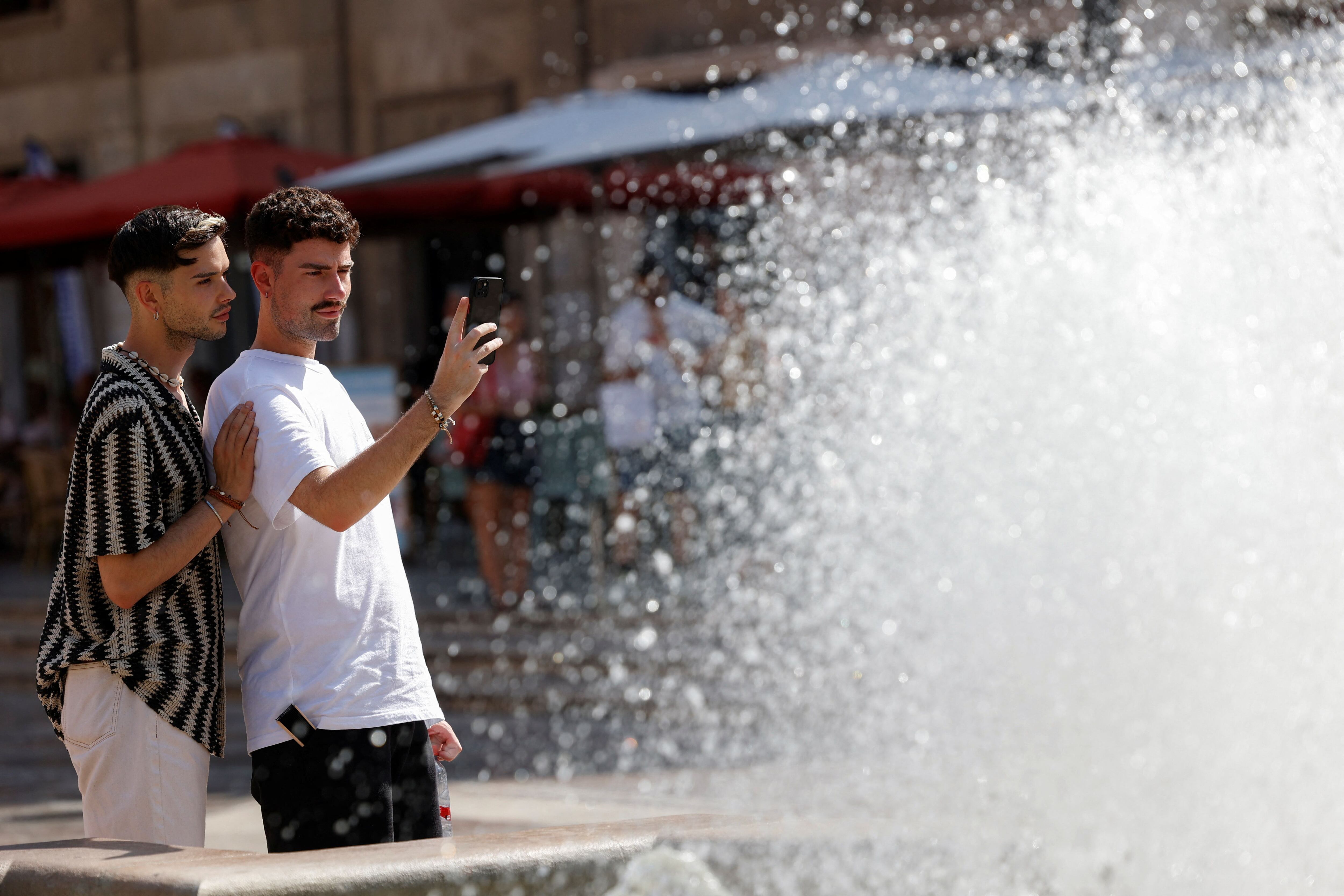 Un par de chicos se toman una selfie en la fuente central de la Plaza de la Virgen durante una ola de calor en Valencia, España 18 de julio 2023. REUTERS/Eva Manez