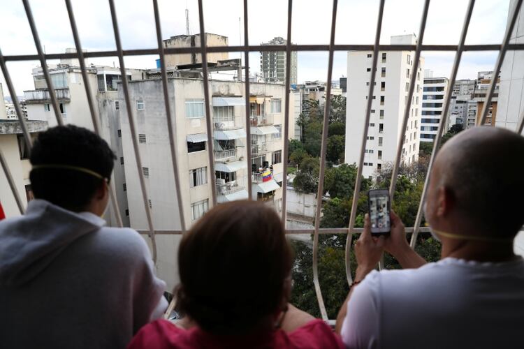 Vecinos en Caracas miran desde su casa mientras el músico Zandu Montoya canta desde el balcón de su vivienda durante la cuarentena nacional por el coronavirus COVID-19 (Reuters)