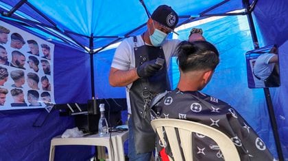 Un venezolano corta el cabello a un hombre en su puesto parte de una feria ambulante (EFE/Martin Alipaz)