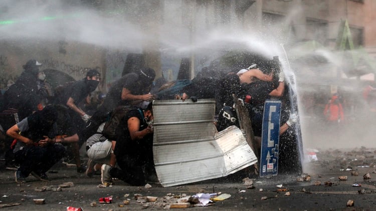 Manifestantes se protegen de la represión durante una manifestación en Chile (Photo by JAVIER TORRES / AFP)
