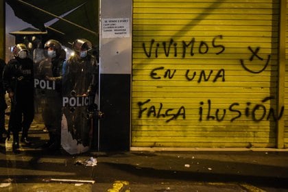 Policías detrás de una pared con una inscripción (AFP)