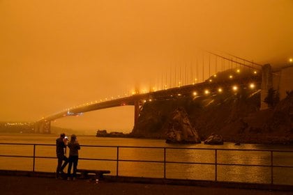 Dos habitantes de Mill Valley, California, toman imágenes del oscuro puente Golden Gate cubierto de humo de los incendios forestales el miércoles 9 de septiembre de 2020, desde un muelle en Fort Baker cerca de Sausalito, California. La foto fue tomada a las 9:47 a.m. de la mañana (AP Photo/Eric Risberg)
