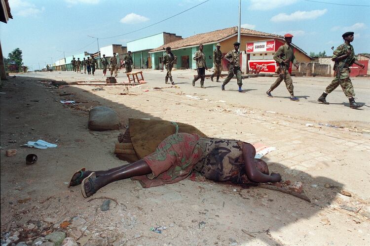 Combatientes del Frente Patriótico caminan el 16 de junio al lado del cuerpo de una mujer asesinada días antes por hutus (AFP)