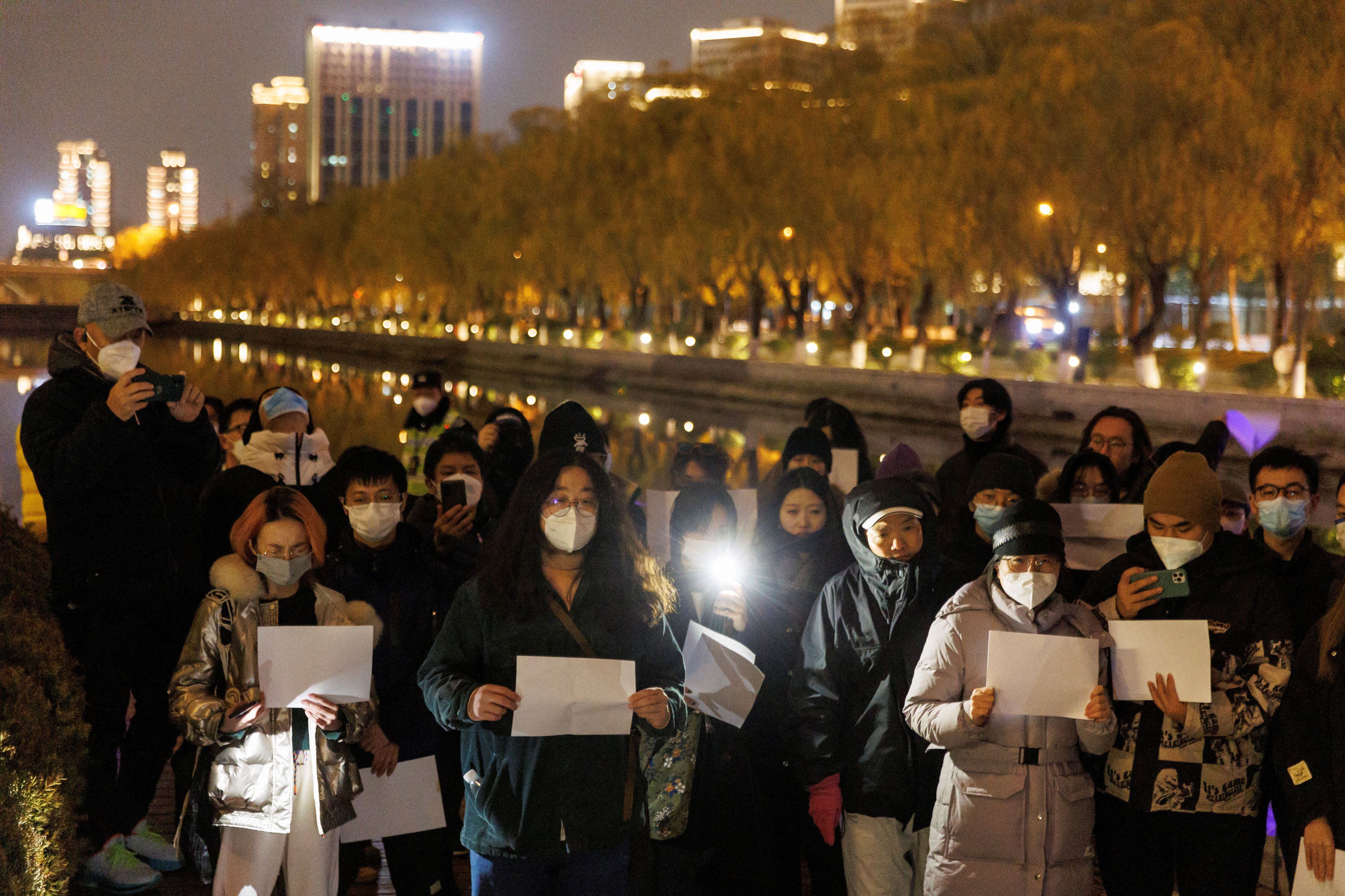 Manifestantes se reúnen para una vigilia y sostiene hojas de papel blanco en protesta por las restricciones de la enfermedad del coronavirus (COVID-19), durante una conmemoración de las víctimas de un incendio en Urumqi, mientras continúan los brotes de COVID-19, en Beijing, China, 27 de noviembre de 2022. REUTERS/Thomas Peter