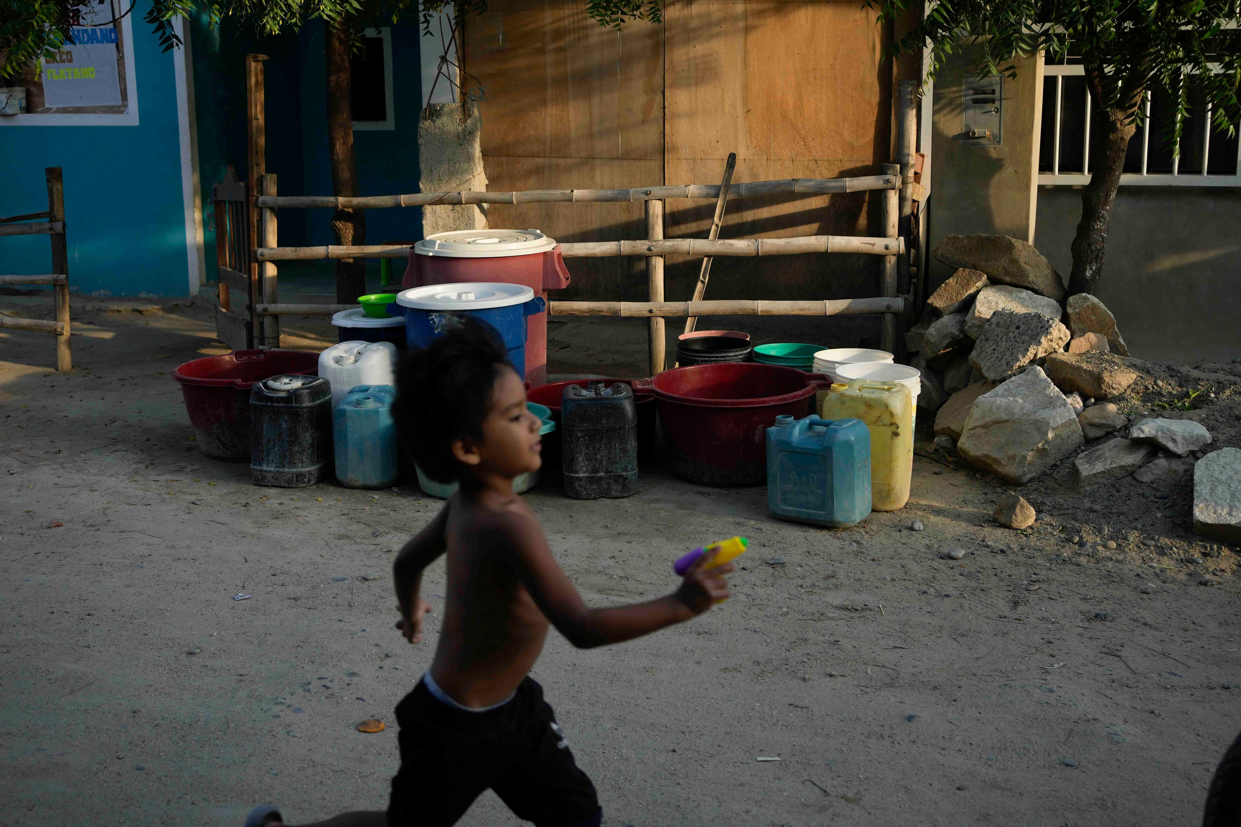 Un niño corre por delante de varios recipientes al frente de una casa, esperando el camión que lleva agua para llenarlos, en el barrio de Los Polvorines de Piura, Perú, el jueves 29 de febrero de 2024. Perú declaró la emergencia de salud en la mayoría de sus regiones el 26 de febrero ante el aumento de casos de dengue. (AP Foto/Martín Mejía)