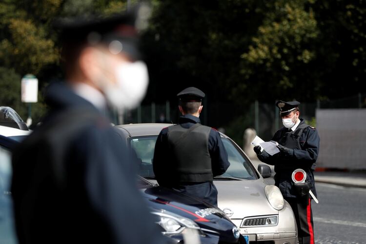 Carabineros italianos con máscaras protectoras verifican si un conductor tiene una razón válida para viajar durante el encierro en Roma, Italia, el 21 de marzo de 2020. (REUTERS/Yara Nardi)