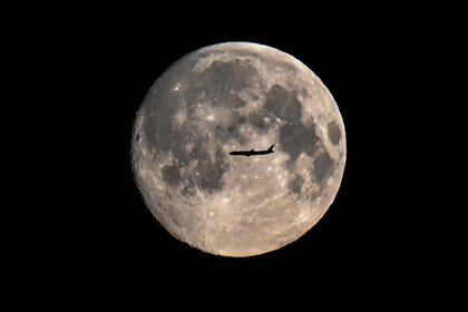 La silueta de un avión se ve frente a la luna en Moscú, el 26 de abril de 2021 (Photo by Kirill KUDRYAVTSEV / AFP)