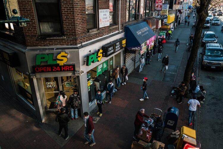 Una larga fila de personas con tapabocas esperan ingresar a PLS, un negocio de transferencias electrónicas y cambio de cheques en Jackson Heights, Queens. (Ryan Christopher Jones / The New York Times)