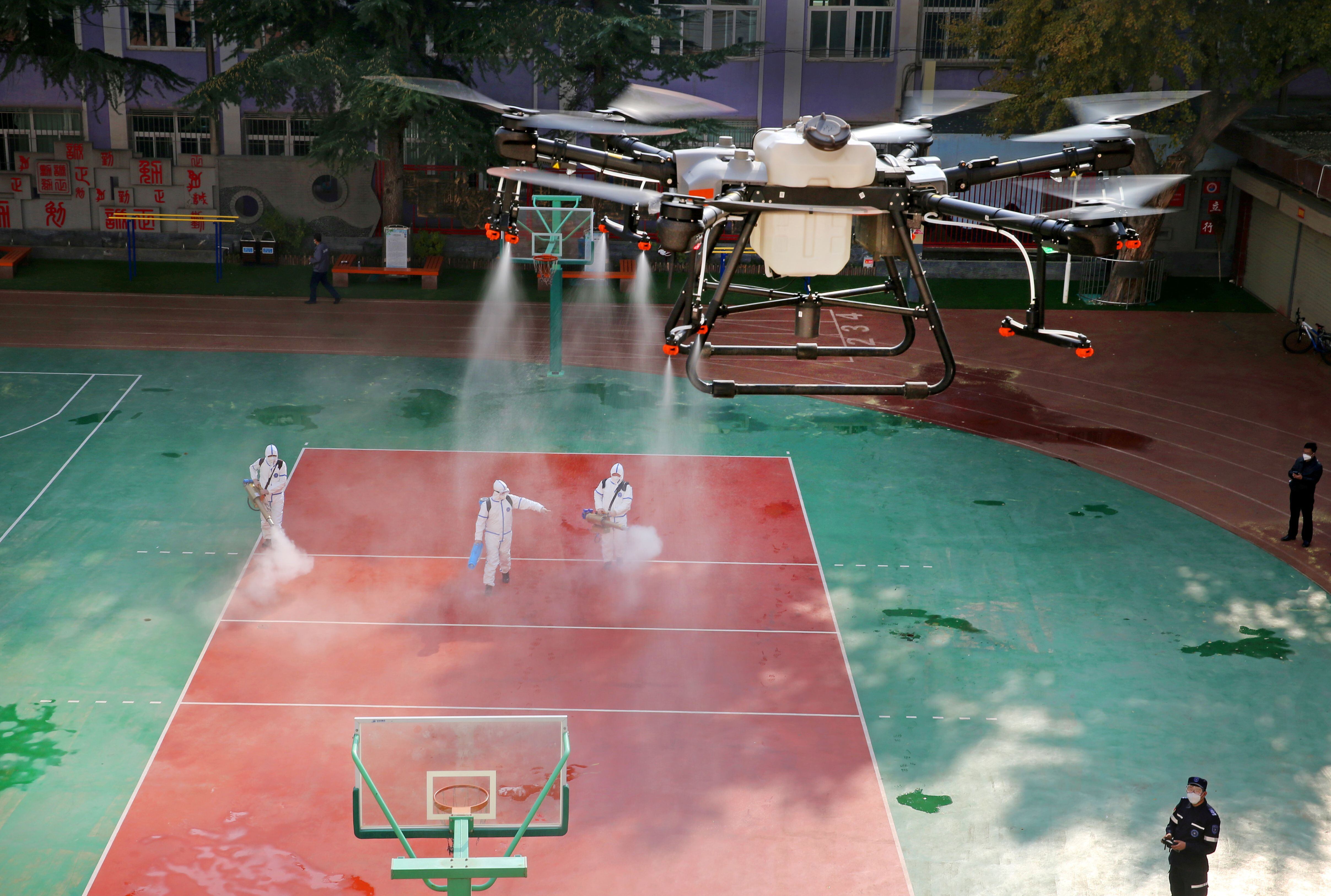 Un dron rocía desinfectante sobre voluntarios que desinfectan una escuela después de casos locales de la enfermedad del coronavirus  en Lanzhou, provincia de Gansu, China, 27 de octubre de 2021. (China Daily via REUTERS)