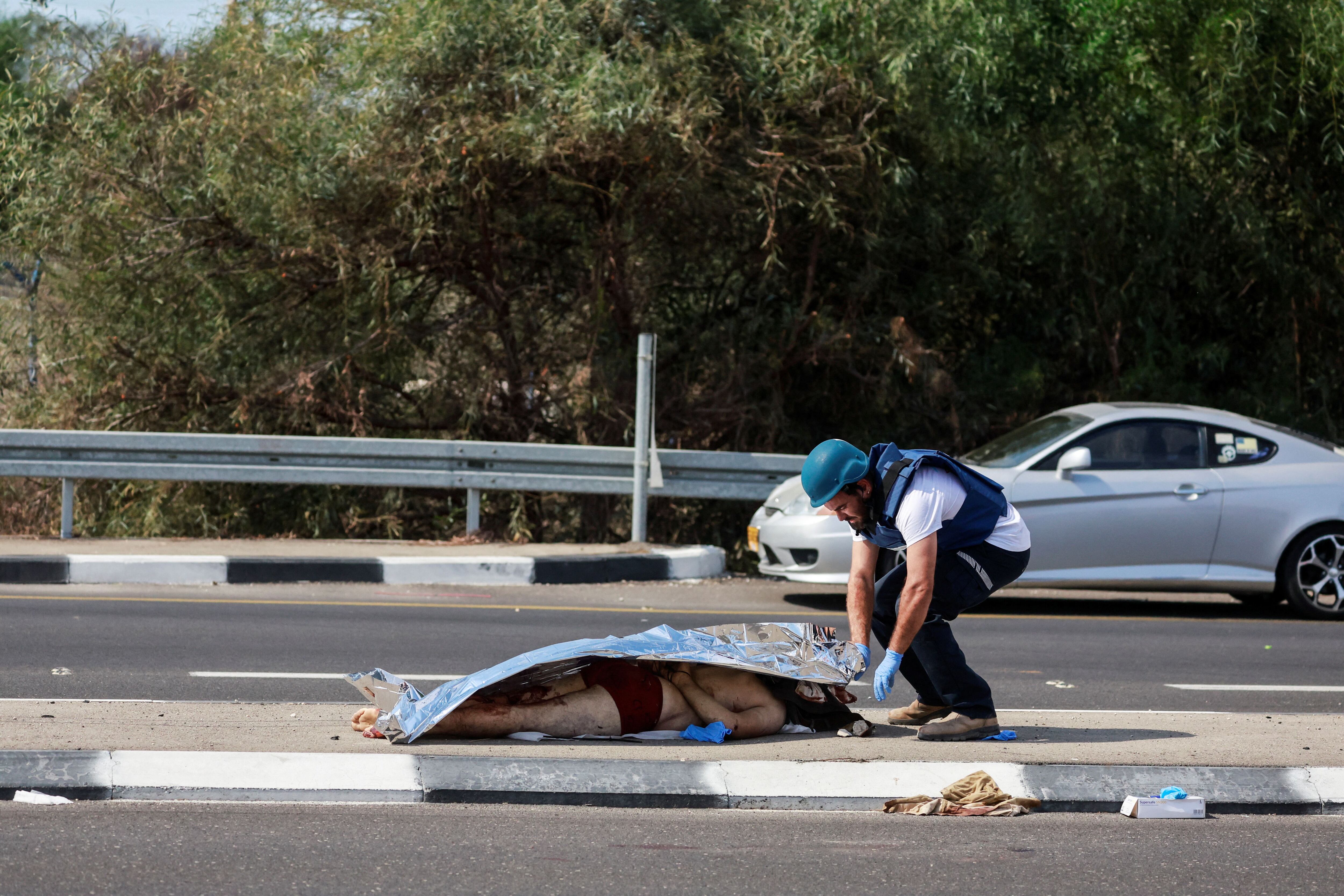 Un paramédico israelí cubre el cuerpo de un israelí asesinado y desnudado en el ataque de hamas (Reuters)