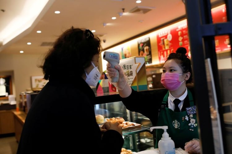 Una trabajadora usa un termómetro para verificar la temperatura de un cliente cuando ingresa a una tienda de Starbucks, mientras el país se ve afectado por un brote del nuevo coronavirus, en Beijing, China. 30 de enero de 2020. REUTERS/Carlos García Rawlins.