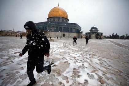 La gente juega junto a la Cúpula de la Roca en el complejo conocido por los judíos como el Monte del Templo y por los musulmanes como el Noble Santuario durante una mañana nevada en la Ciudad Vieja de Jerusalén, el 18 de febrero de 2021. REUTERS / Ammar Awad