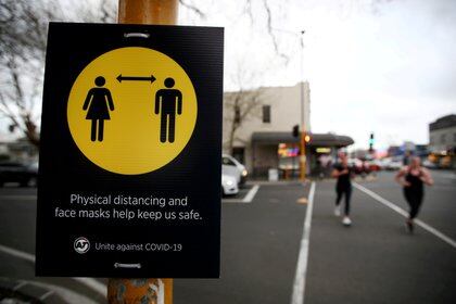 FILE PHOTO: FILE PHOTO: People jog past a social distancing sign on the first day of New Zealand's new coronavirus disease (COVID-19) safety measure that mandates wearing of a mask on public transport, in Auckland, New Zealand, August 31, 2020.  REUTERS/Fiona Goodall//File Photo