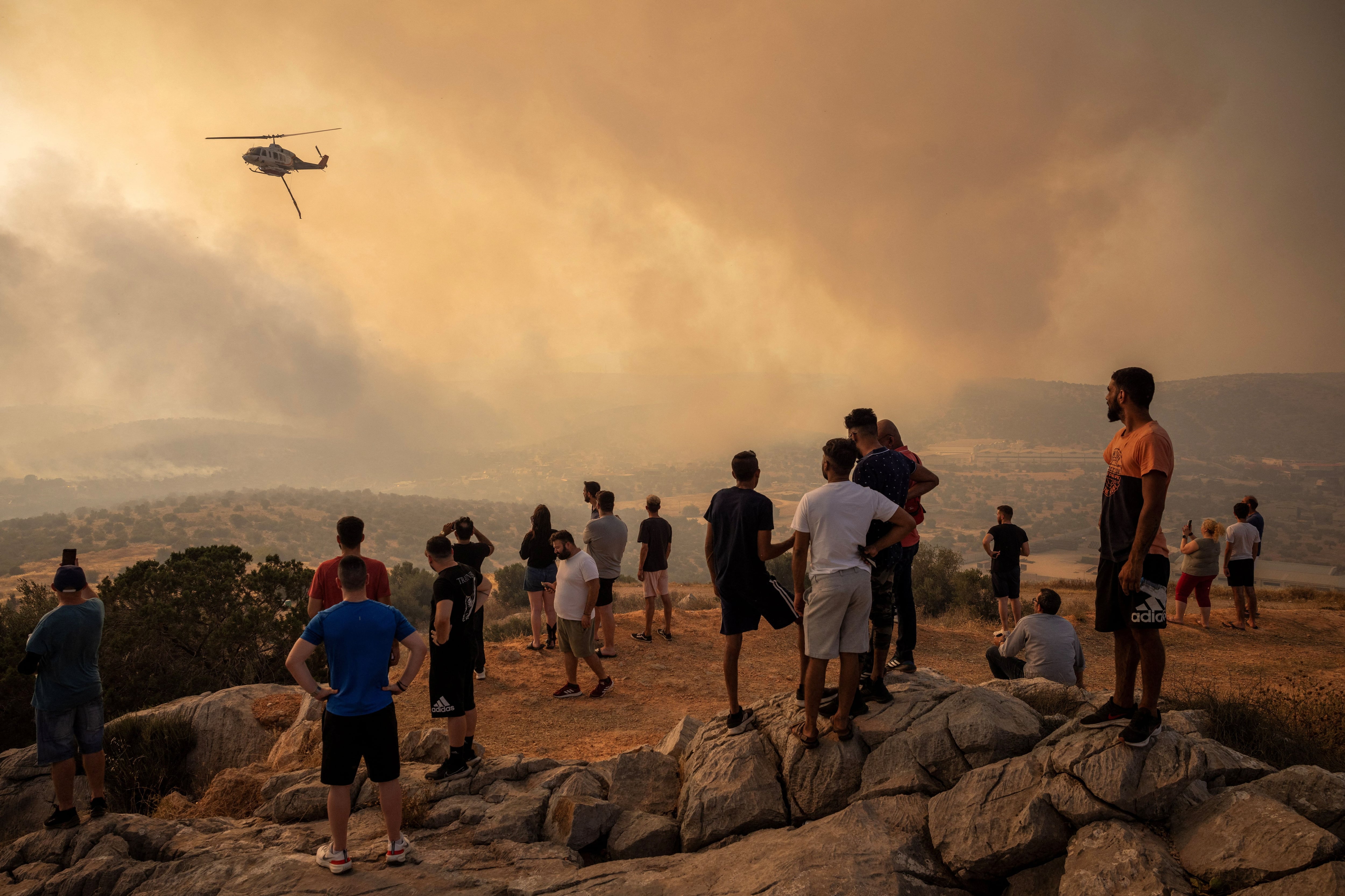 Varias personas observan un helicóptero de extinción de incendios tras lanzar agua mientras arde un incendio forestal en Mandra, Grecia, 18 de julio de 2023. REUTERS/Alkis Konstantinidis