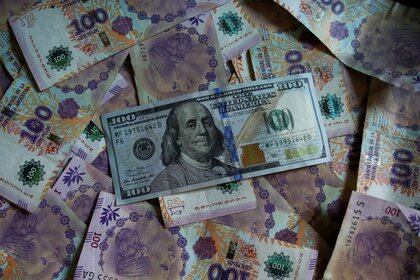 Un billete de cien dólares estadounidenses reposa sobre billetes de cien pesos de Argentina, cuando tenían el mismo valor (Reuters)