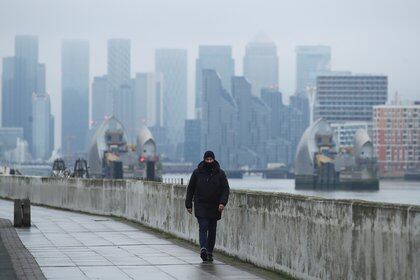 Edificios en el distrito comercial de Canary Wharf, mientras un hombre con tapabocas camina por un sendero en Londres el 27 de enero de 2021. REUTERS/Peter Cziborra