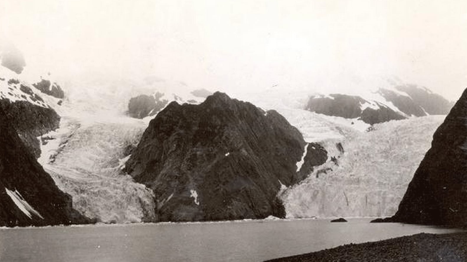 <p>La fotografía de 1909&nbsp;muestra al Glaciar Holgate, de marea en la cabecera del fiordo, con el Pequeño Glaciar de Holgate, uno de sus antiguos afluentes , situado a su izquierda. No hay vegetación presente</p><p></p><p></p> usgs.gov 163