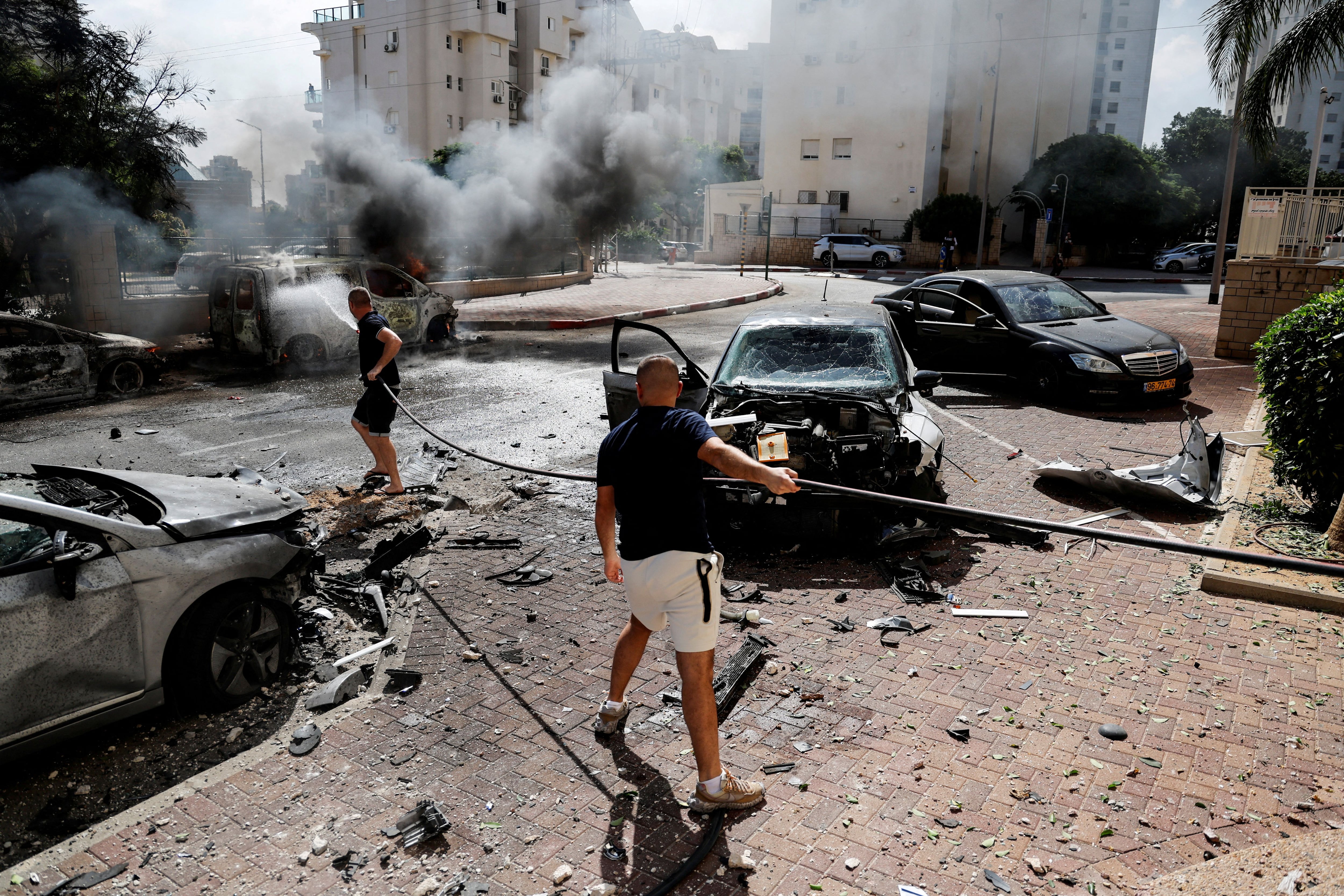 Varias personas trabajan para apagar un incendio que envuelve una furgoneta, mientras se lanzan cohetes desde la Franja de Gaza, en Ashkelon, sur de Israel (REUTERS/Ammar Awad)