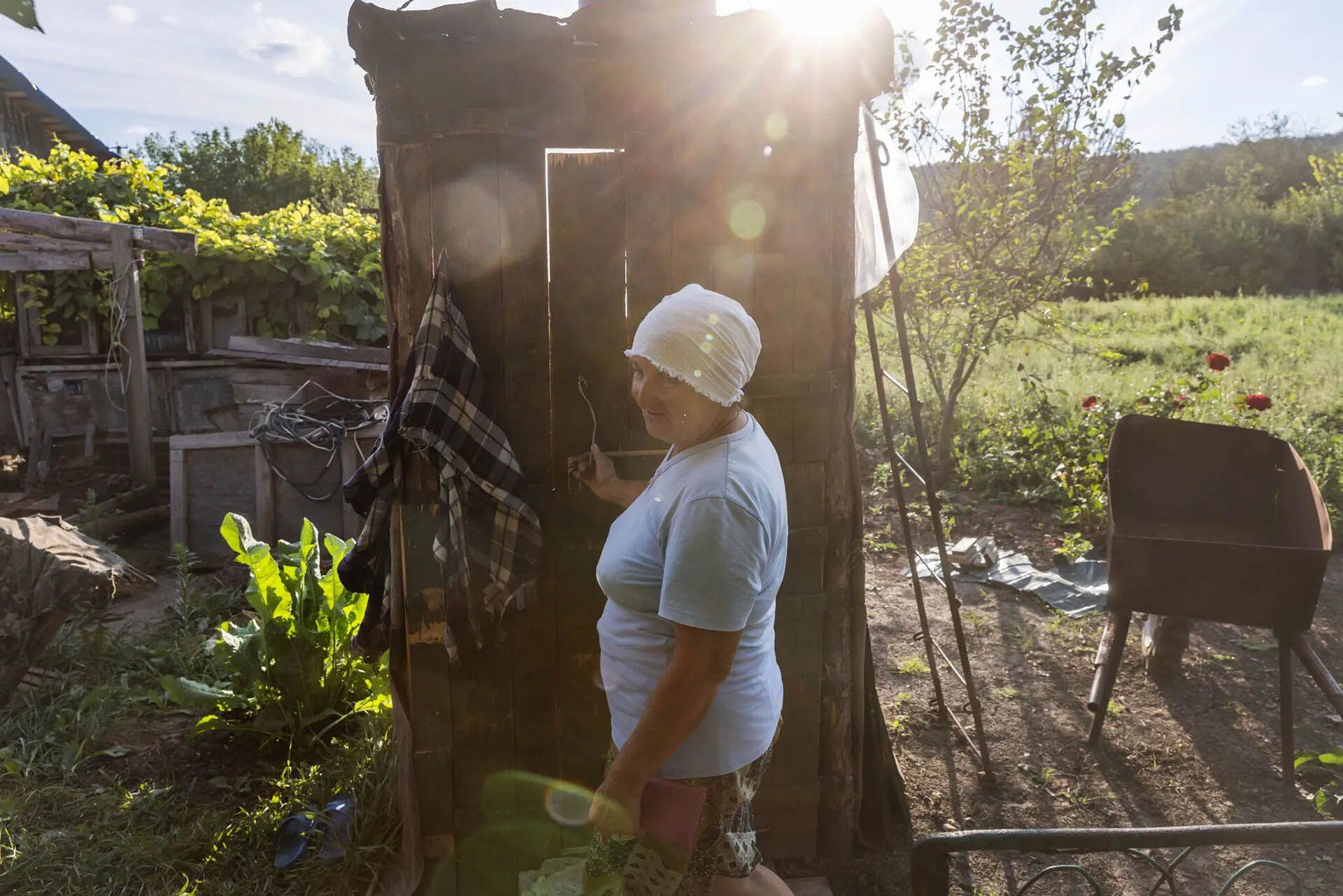 La Sra. Huk cerca de una ducha al aire libre que su hijo construyó con cajas de municiones rusas (David Guttenfelder para The New York Times)