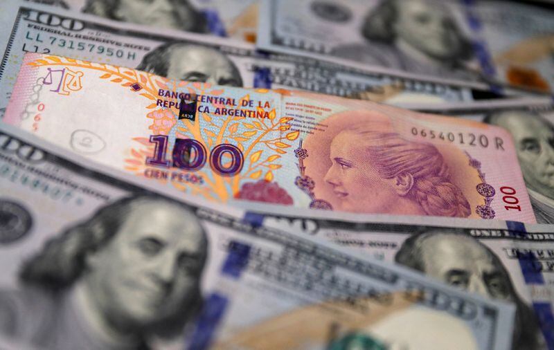 Foto de archivo - Un billete de devaluados 100 pesos argentinos sobre otros de dólares estadounidenses, a modo ilustrativo. Oct 17, 2022. REUTERS/Agustin Marcarian/