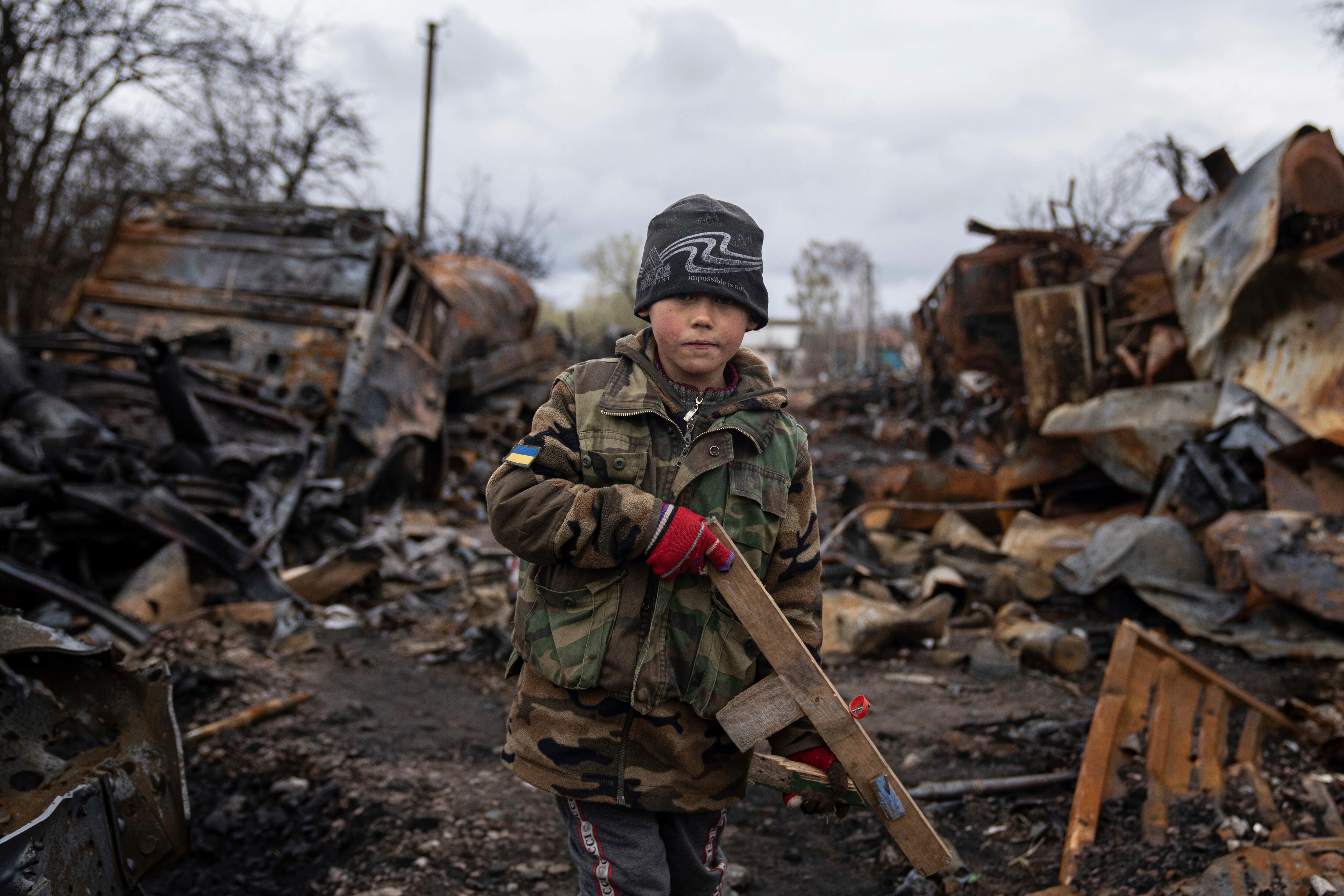 Yehor, de 7 años, sostiene un rifle de juguete de madera junto a vehículos militares rusos destruidos cerca de Chernihiv, Ucrania, el domingo 17 de abril de 2022.