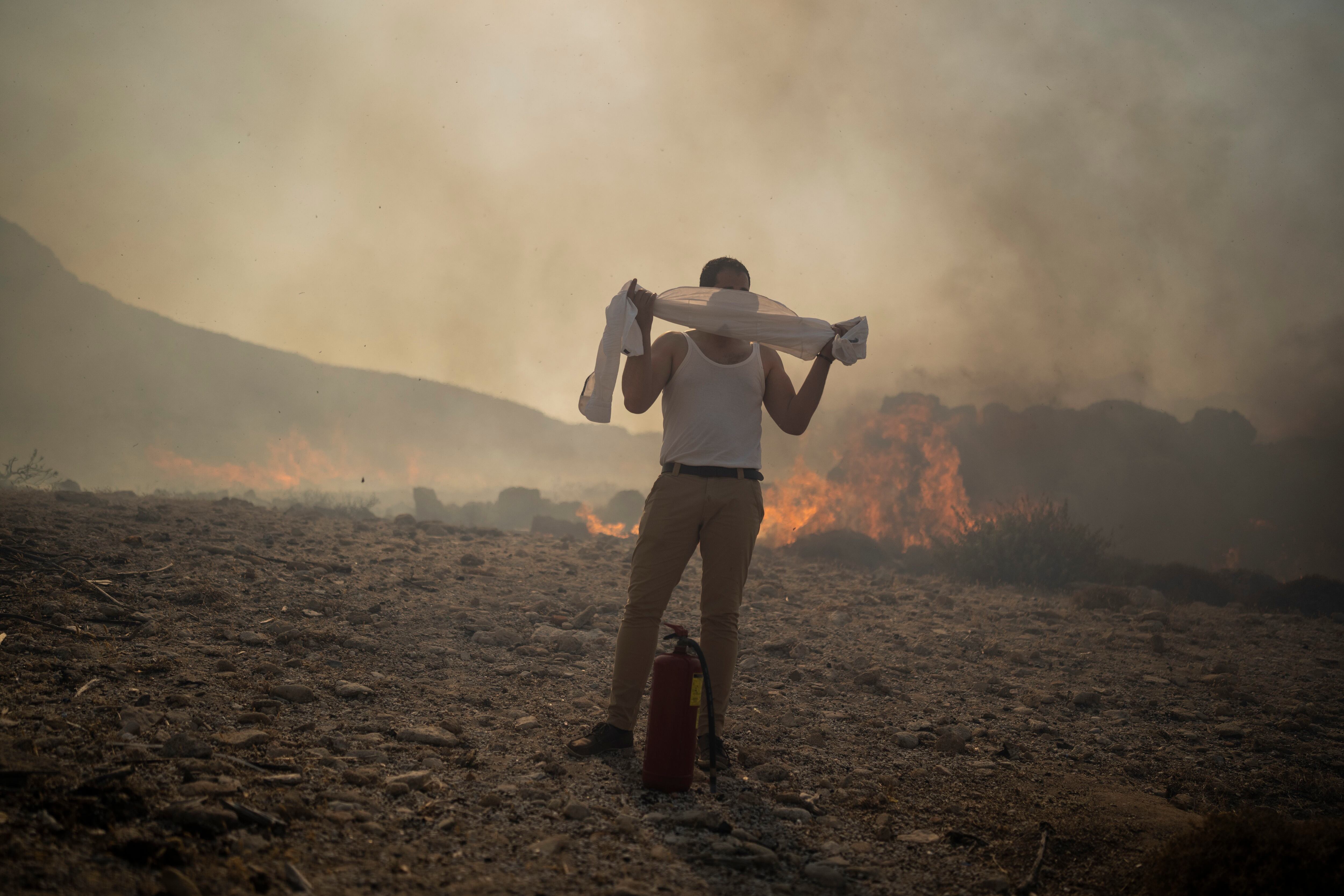 Un hombre se tapa el rostro con su camisa mientras trata de extinguir un incendio cerca del balneario costero de Lindos (AP Foto/Petros Giannakouris)