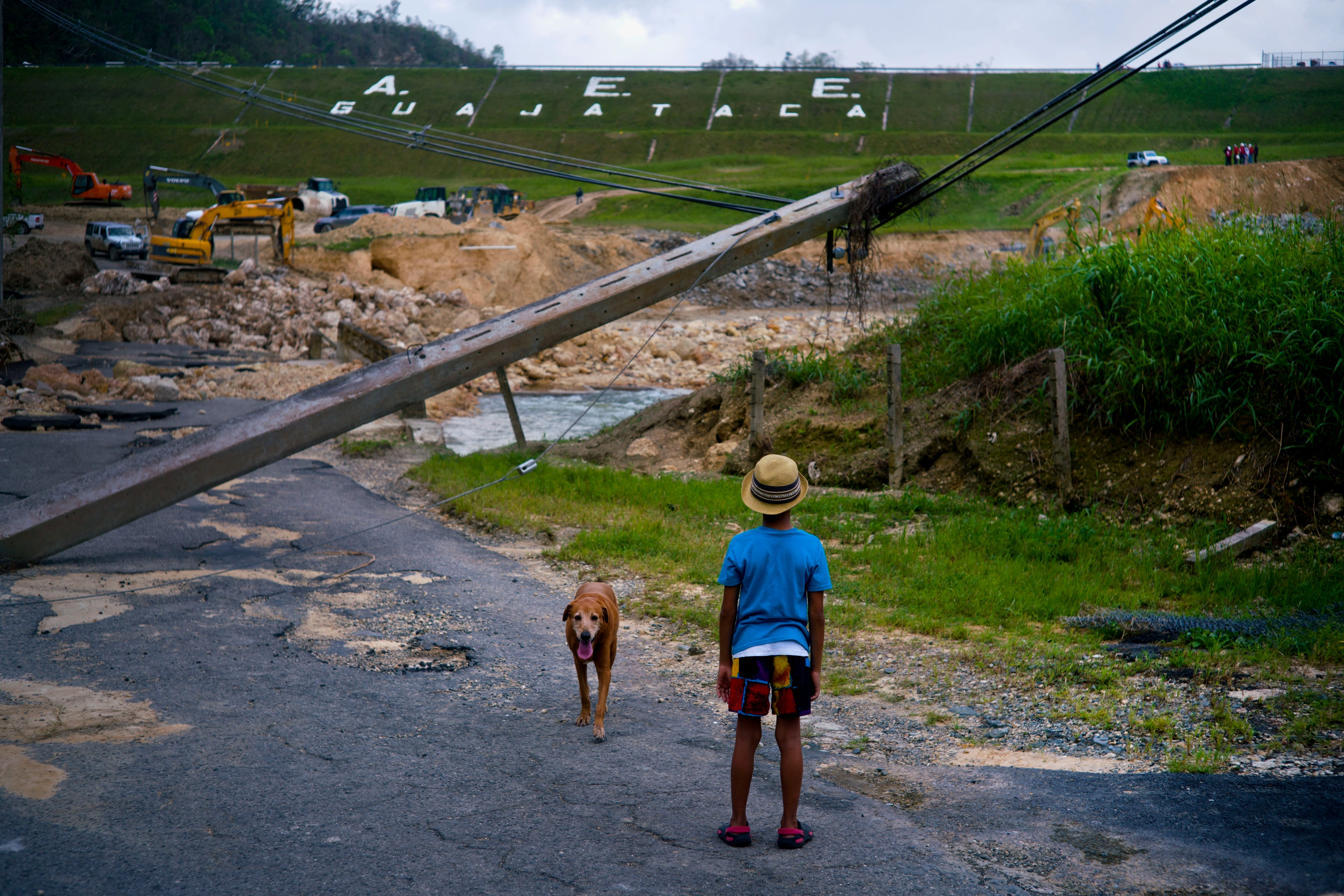  Un niño acompañado por su perro observa el martes 17 de octubre de 2017 las labores de reparación de la represa Guajataca, que fue dañada por el huracán María, en Quebradillas, Puerto Rico. (AP Foto/Ramon Espinosa, Archivo)