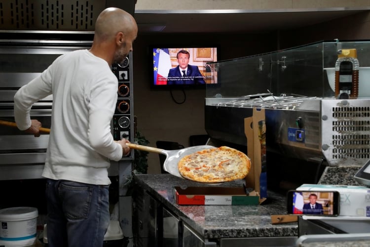 El presidente francés Emmanuel Macron se dirige a la nación sobre el brote del coronavirus, en una pantalla de televisión en una pizzería para llevar en Niza, Francia (Reuters)