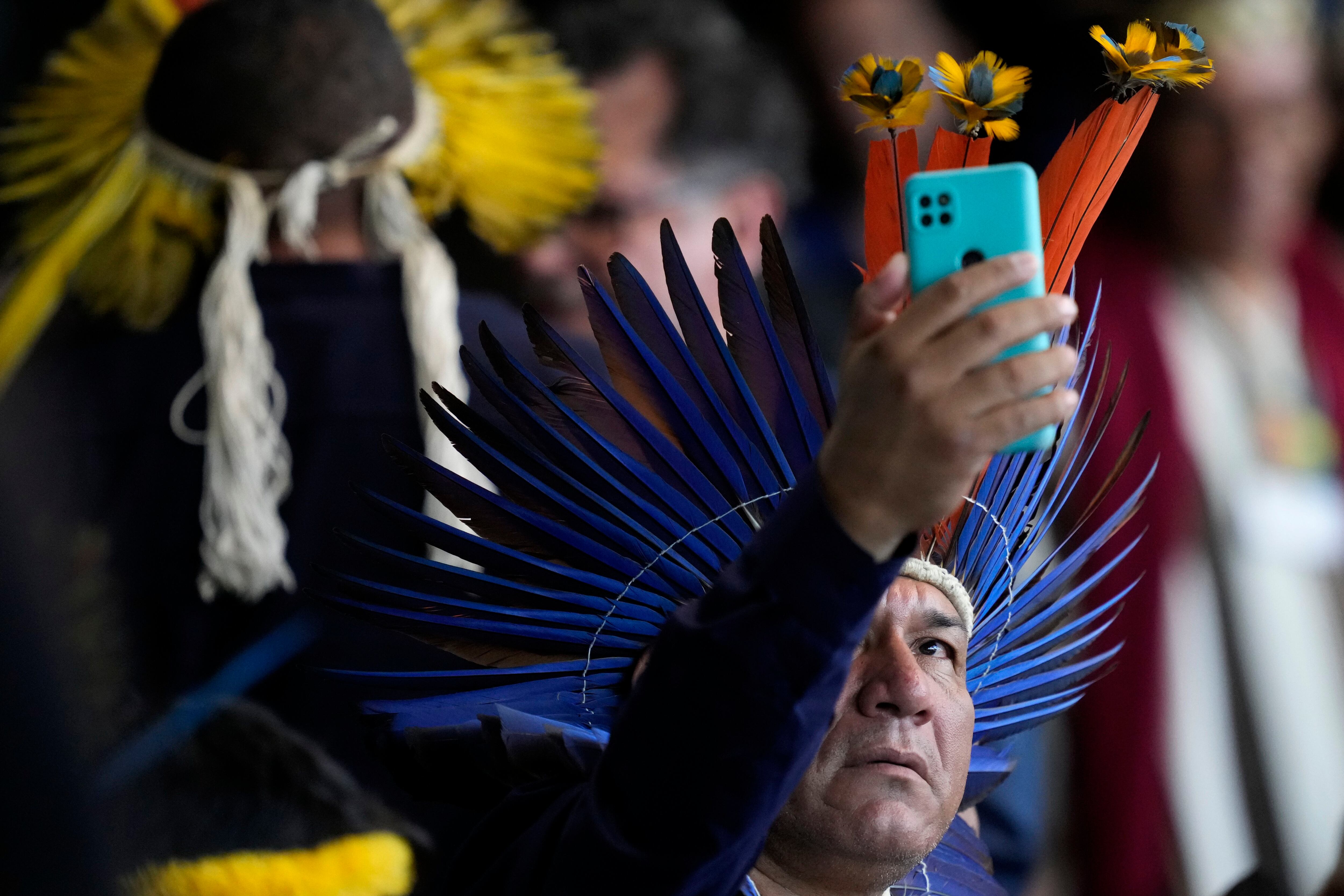 Un indígena toma una fotografía con su celular mientras espera el inicio de la ceremonia de clausura de la primera reunión ordinaria del Consejo Nacional para Políticas Indígenas, en Brasilia, Brasil, el 18 de abril de 2024 (AP Foto/Eraldo Peres)