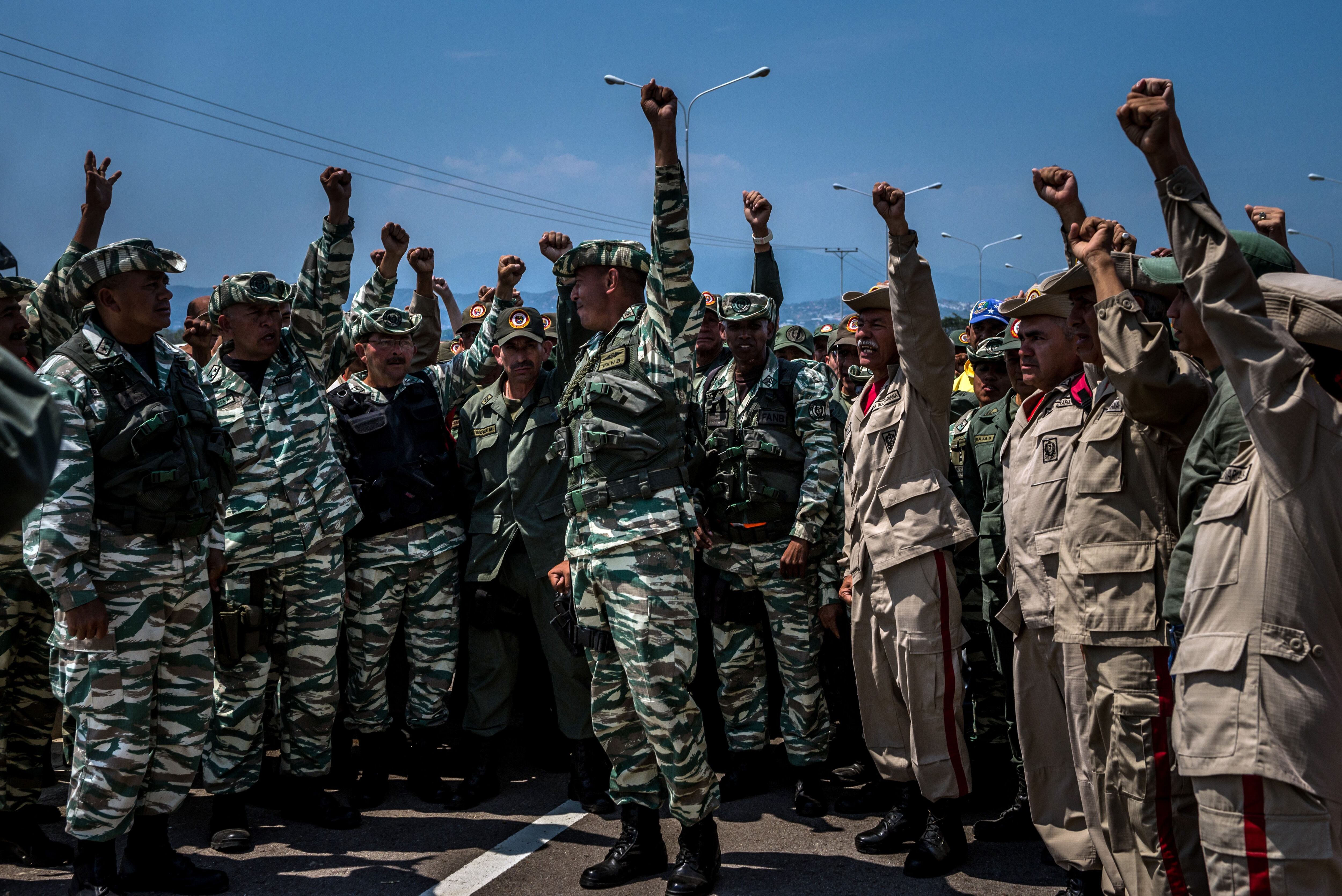 Soldados venezolanos y miembros de la milicia alzan sus puños cerca del puente que conecta Venezuela y Colombia para que los medios del Estado graben mientras demuestran su apoyo al presidente Nicolás Maduro. (Meridith Kohut para The New York Times)