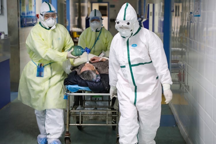 Trabajadores en trajes protectores trasladan a un paciente en una sala aislada de un hospital del distrito de Caidian, provincia de Hubei (China Daily via REUTERS)