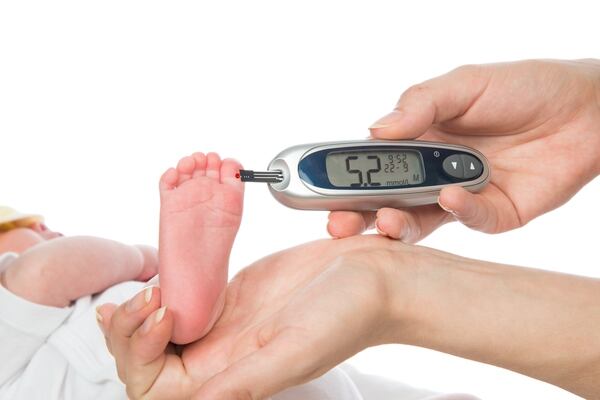 Doctor hand measuring glucose level blood test from diabetes patient child baby feet using glucometer and small drop of blood