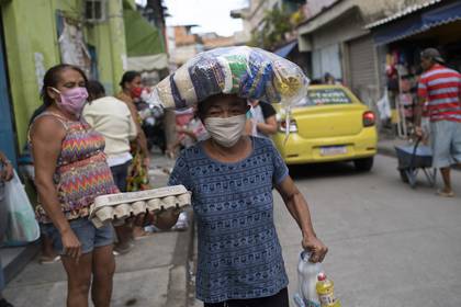 Maria Rita Dias dos Santos, con mascarilla de protección, lleva a su casa comida donada por antiguos presos que participan en una organización sin fines de lucro, que da alimentos a personas que están pasando problemas por la pandemia del nuevo coronavirus, en la favela de Para-Pedro, en Río de Janeiro, Brasil, el viernes 8 de mayo de 2020. (AP Foto/Silvia Izquierdo)