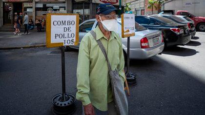 Un hombre de la tercera edad camina  junto a un aviso de venta de pollo a 10 dólares, en Caracas (EFE)