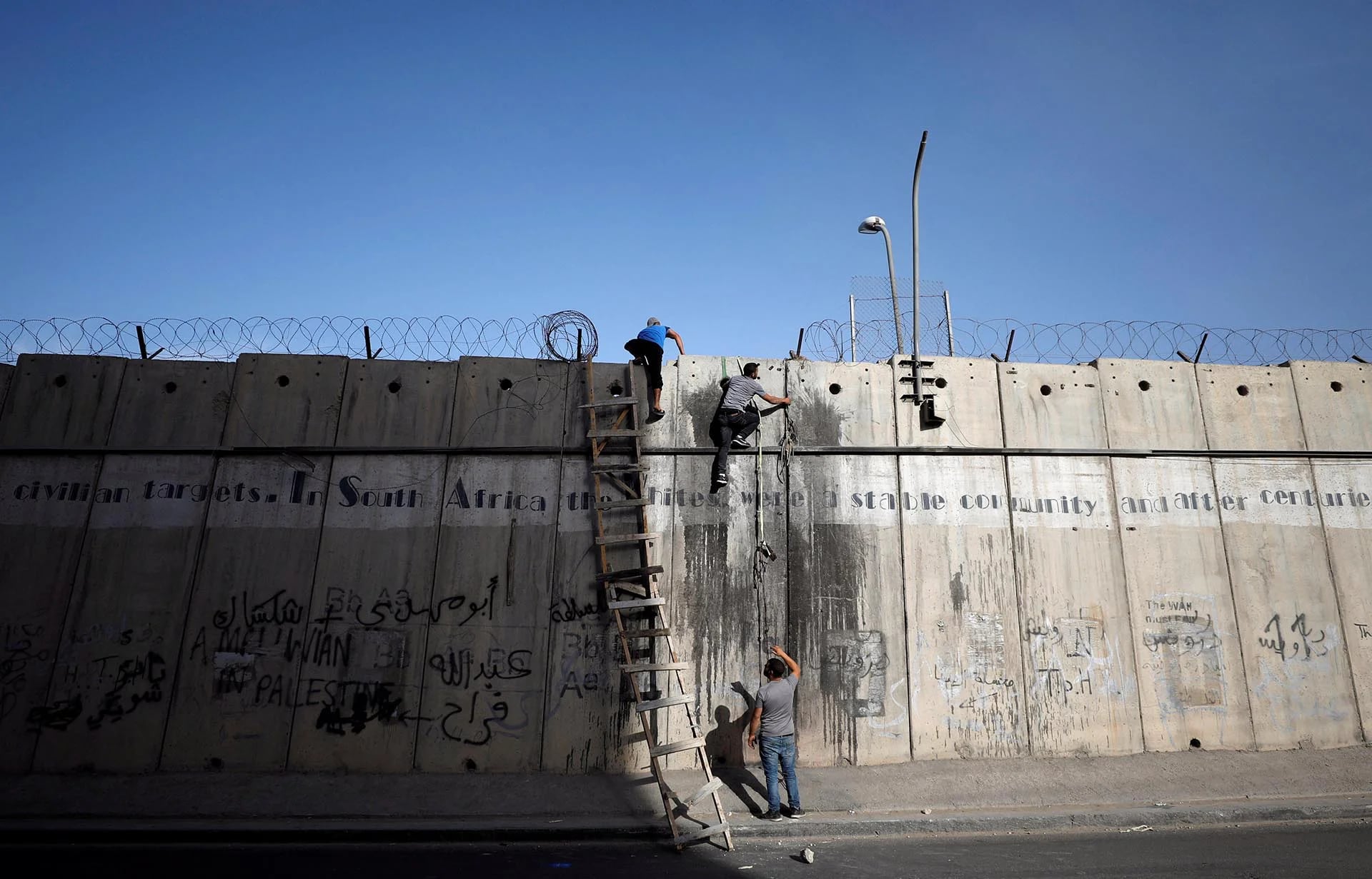 Palestinos escalan una sección de la controvertida barrera israelí mientras tratan de hacer su camino para asistir a las oraciones del Ramadán en la mezquita de Jerusalén, cerca de Ramallah