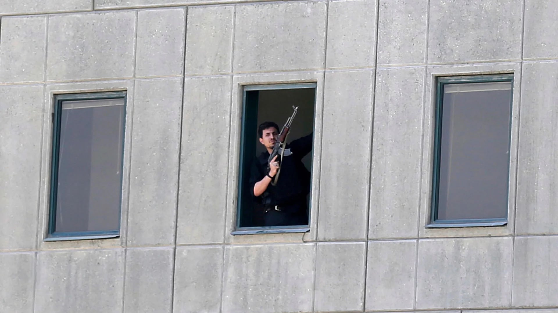 Un hombre armado mira desde una de las ventanas del Parlamento de Irán (AP)