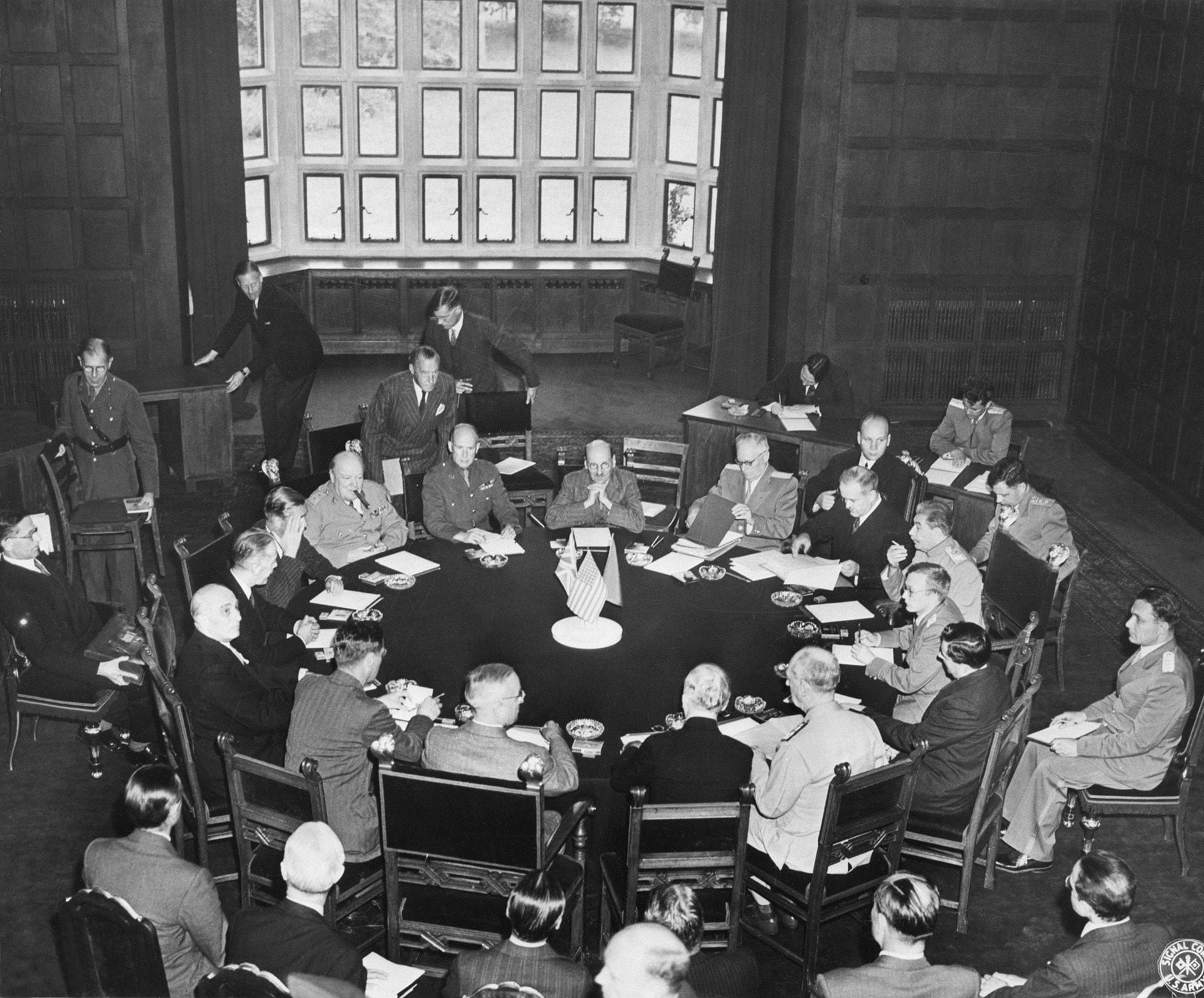 La conferencia de los tres grandes comienza en una sala del palacio de Potsdam, Alemania. El presidente Harry S. Truman está sentado de espaldas a la cámara, con asistentes a cada lado; el mariscal Joseph Stalin está sentado más a la derecha, mientras que el primer ministro Winston Churchill y su personal están a la izquierda (Getty Images)