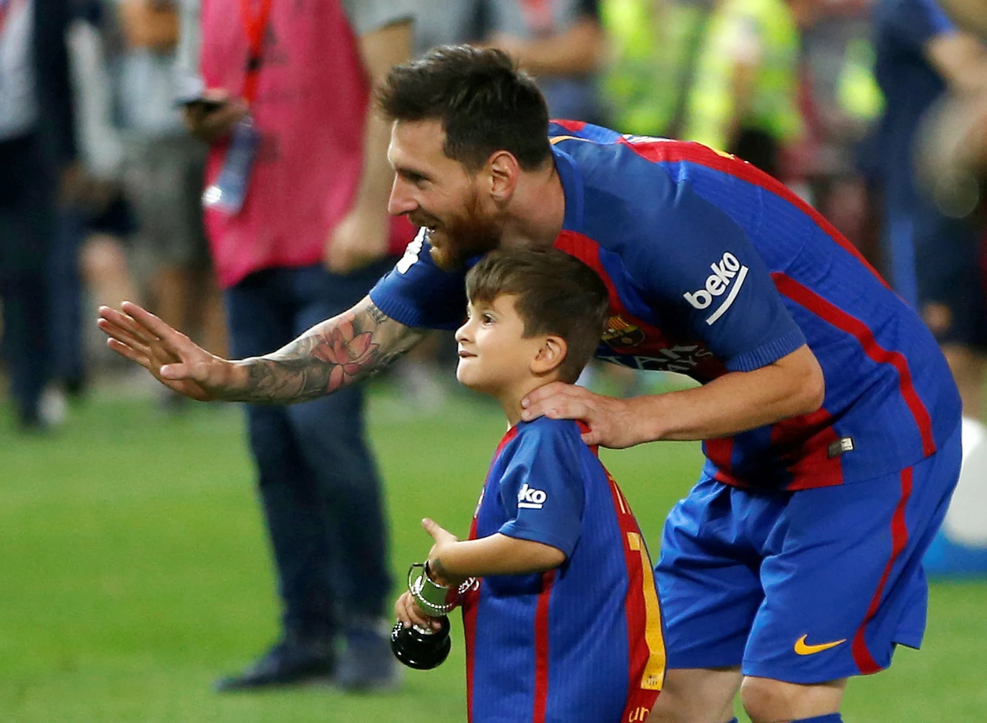 Lionel y Thiago Messi saludan a cámara. El pequeño porta una réplica mini de la copa que se llevó el primer equipo del Fútbol Club Barcelona