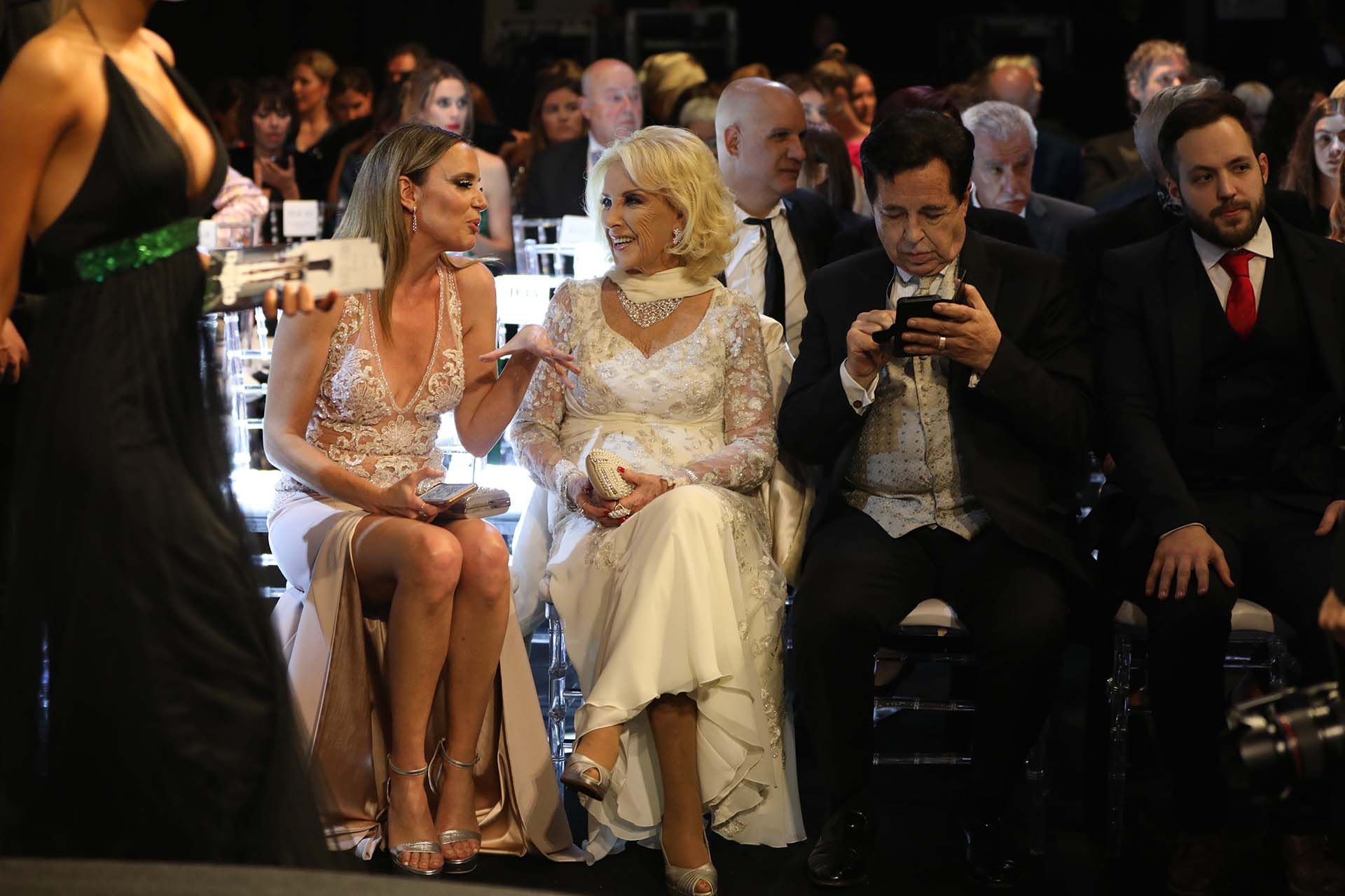 Mirtha -esplénida en nude con un vestido de los hermanos Iara- se ríe junto a Soledad Villarreal -en un Cosano con tajo y transparencias- que se acercó especialmente para hablar con la diva. La dueña de los almuerzos contó: “Yo me pruebo la ropa un día a la semana, con Vidal Rivas elegimos los modelos, cada vez que tengo más años soy más coqueta, quiero que sepan que esta fiesta es maravilosa y que sería bueno que apoyen un poco a la industria textil, que está pasando momentos muy delicados. Este Gobierno, o el que venga, que ayuden a la industria textil. Muchas gracias, esta noche va a ser inolvidable”