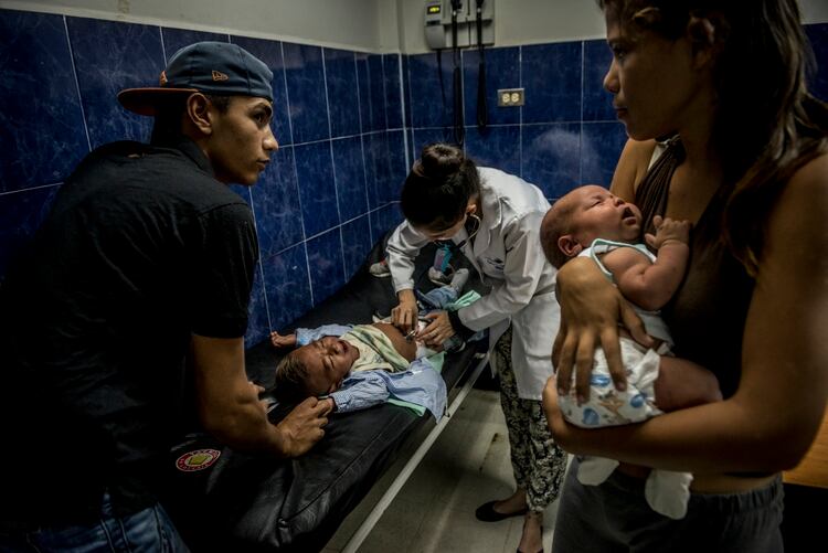Alejandra Urquiola carga a su bebé mientras su pareja, Yonathan Graterol, observa cómo los médicos atienden a su hijo de un año, Yosneider. (Meridith Kohut/The New York Times)