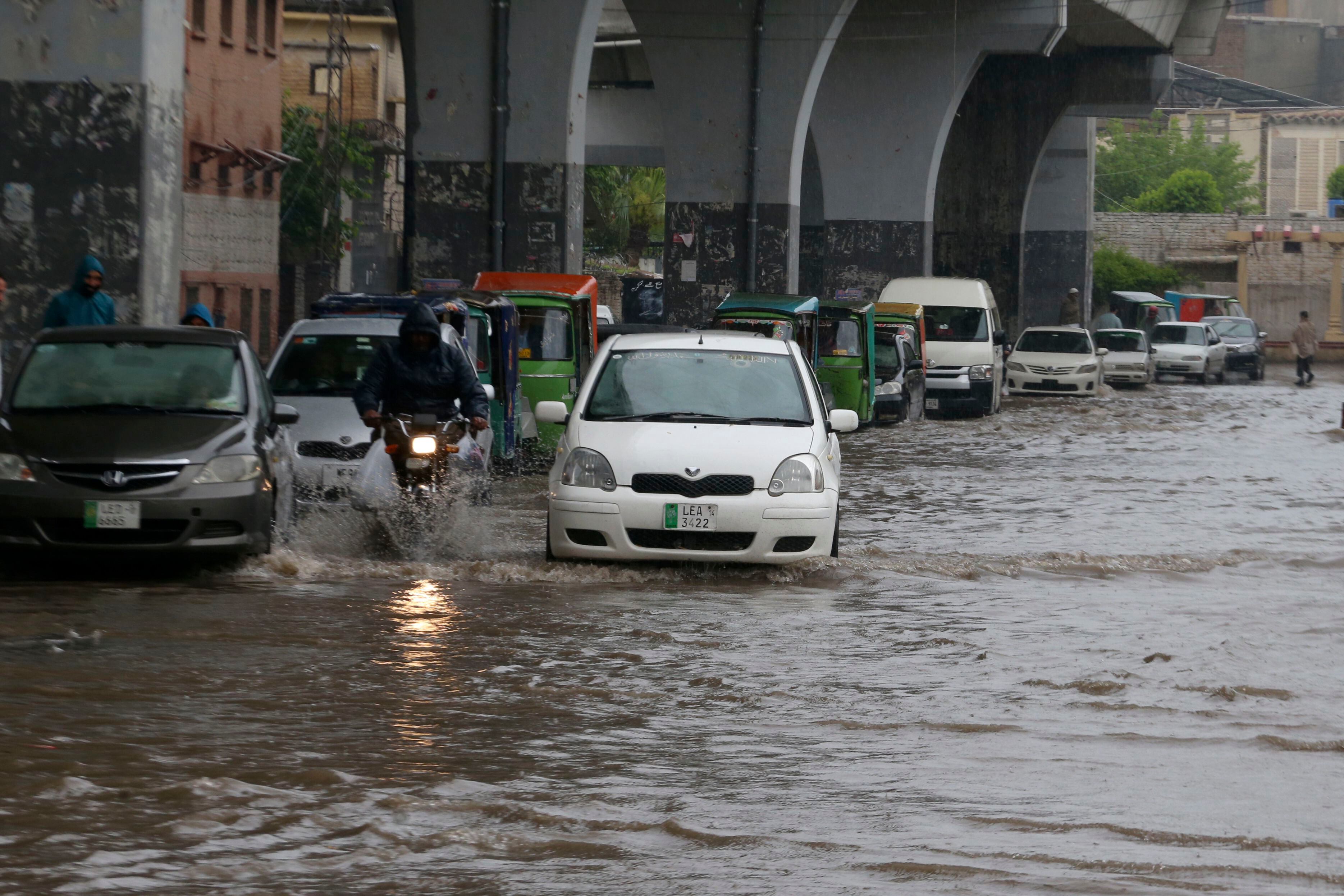 Un conductor en moto y un auto circulan por una calle inundada por las fuertes lluvias en Peshawar, Pakistán, el lunes 15 de abril de 2024. Docenas de personas, la mayoría agricultores, murieron en Pakistán debido a las precipitaciones en los últimos tres días, según dijeron las autoridades el lunes. (AP Foto/Muhammad Sajjad)